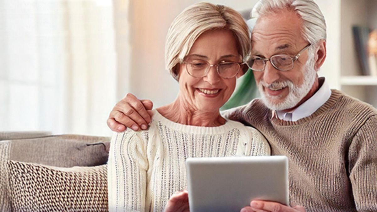 Starszy mężczyzna przytulony i obejmujący ramieniem kobietę, razem wpatrzeni w tablet