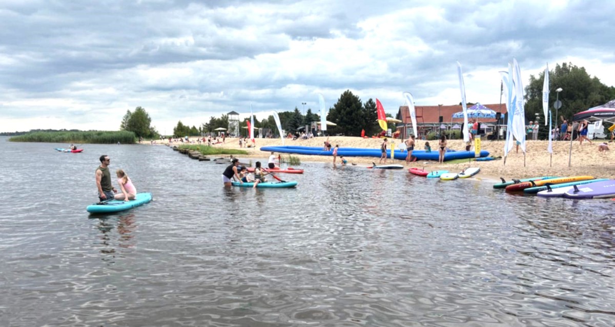 Widok na plażę od strony wody. Dzieci pływające na SUP