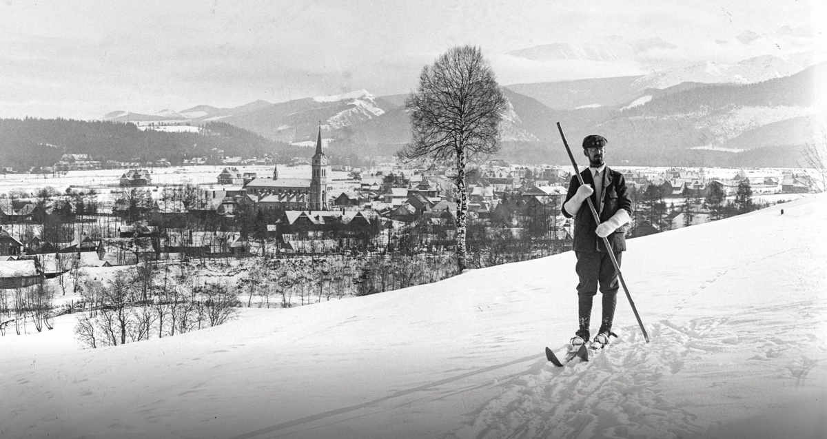 Zdjęcie archiwalne narciarz na stoku góry odpychający się jednym kijem - w tle zabudowania