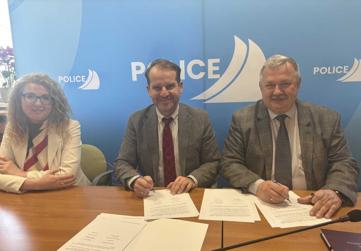 Kobieta i dwóch mężczyzn siedzi za stołem. Mężczyźni podpisują dokumenty