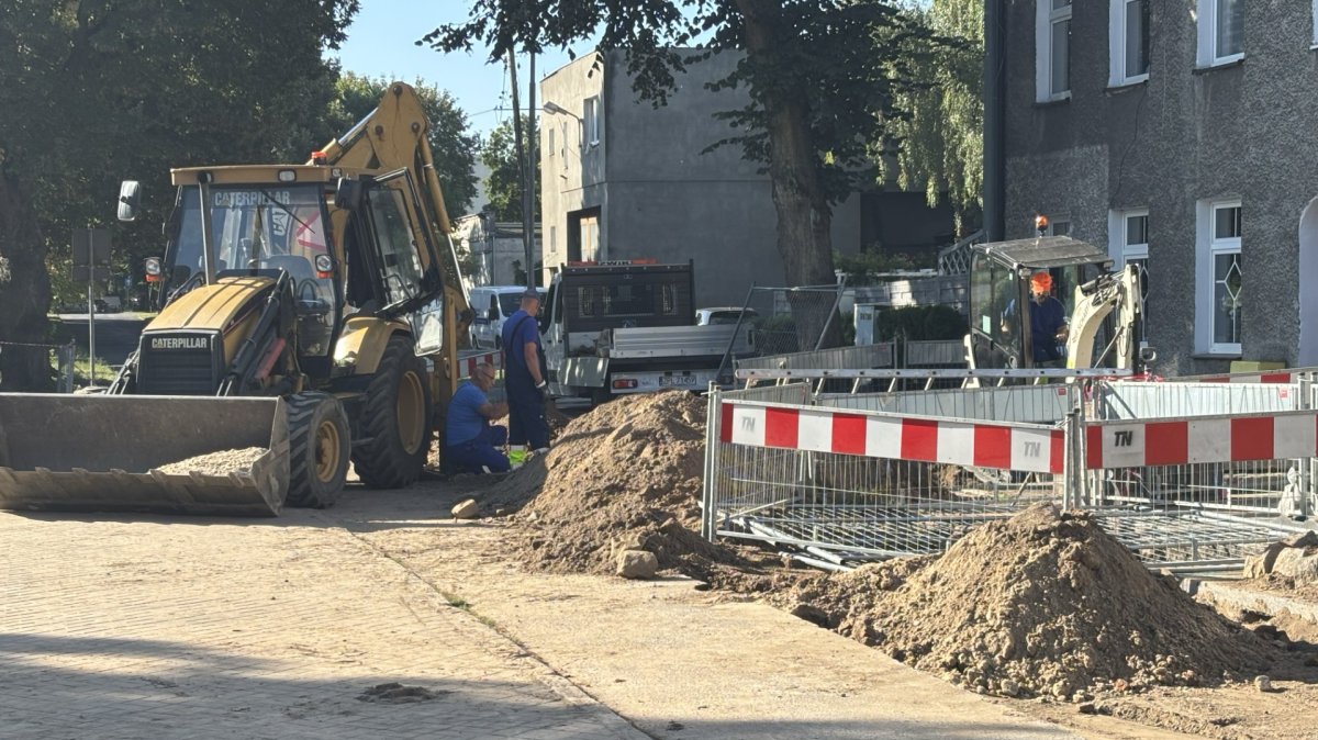 Po prawej stronie zdjęcia wykop ogrodzony barierkami, po lewej stoi koparka
