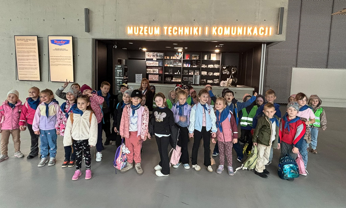 Grupa dzieci pozuje do zdjęcia, w tle napis Muzeum Techniki i Komunikacji