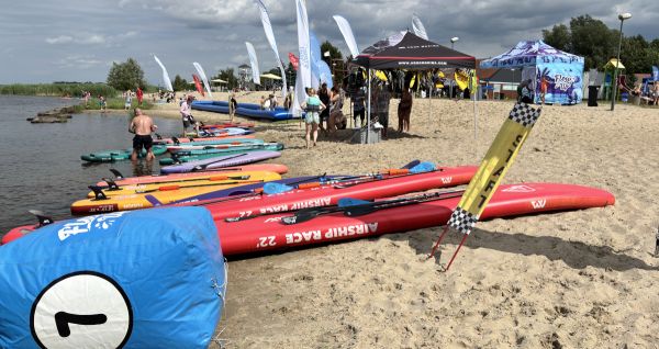 Na plaży leżą deski i sprzęt wodny, w tle osoby