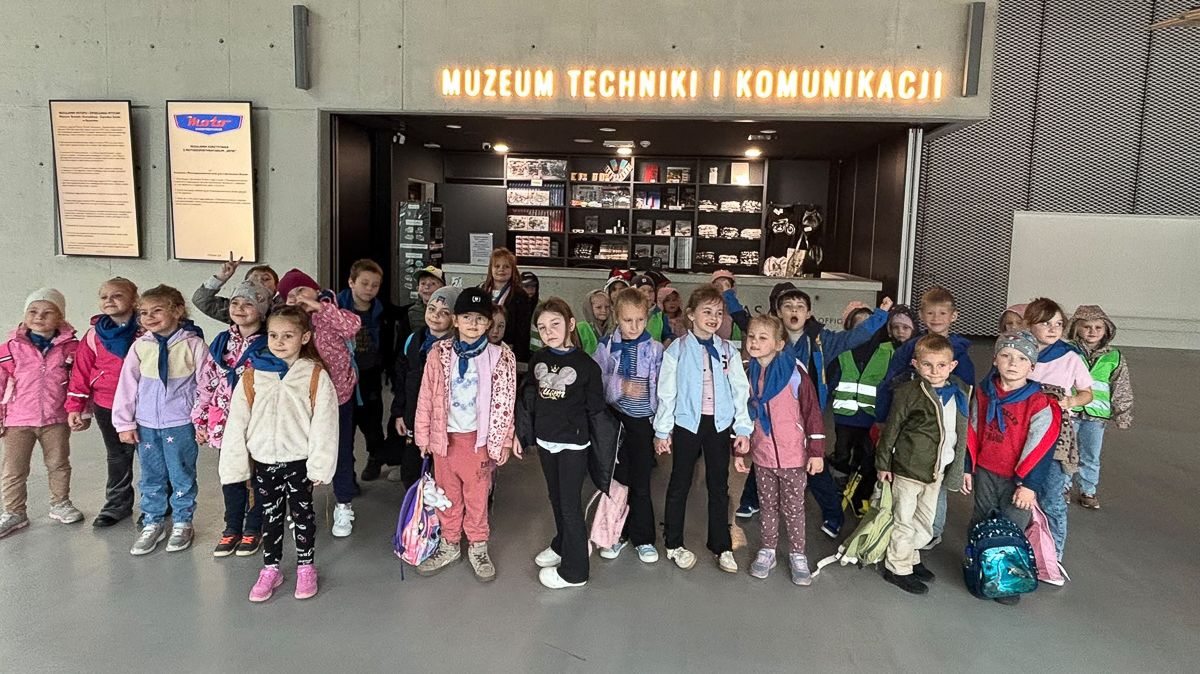 Grupa dzieci pozuje do zdjęcia, w tle napis Muzeum Techniki i Komunikacji