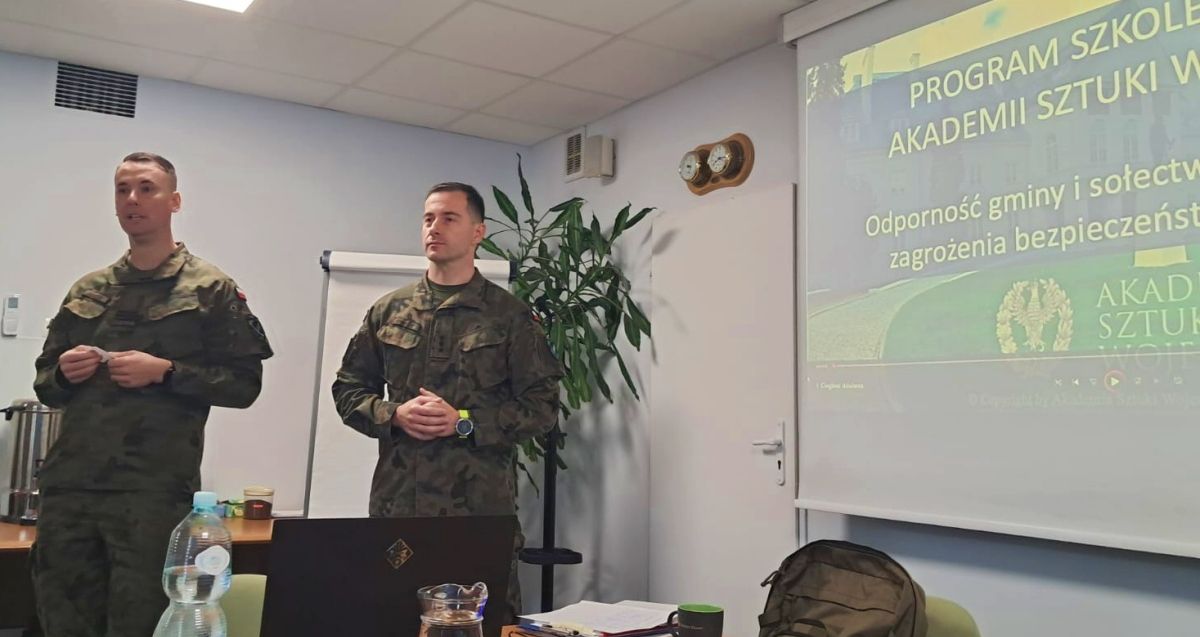 Dwóch mężczyzn w mundurach wojskowych stoi, lewej strony wyświetlana prezentacja