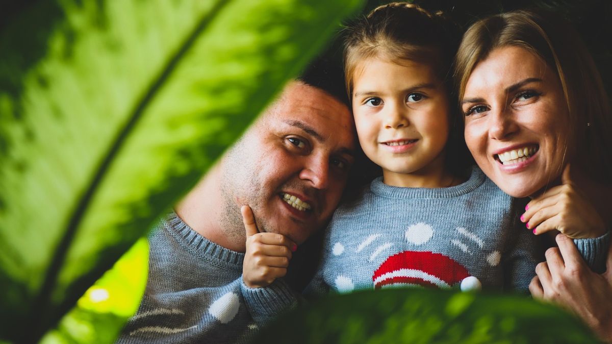 Trzy osoby na zdjęciu dziecko wraz z rodzicami. Część zdjęcia przysłonięta liściem