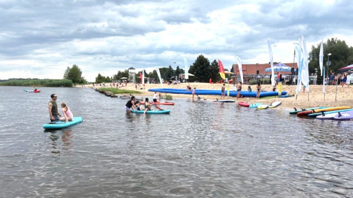 Widok na plażę od strony wody. Dzieci pływające na SUP