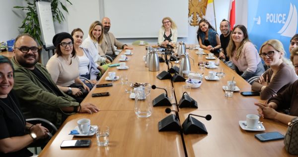 Osoby siedzą przy dużym stolę, patrzą w stronę osoby fotografującej