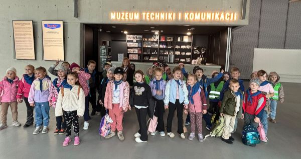 Grupa dzieci pozuje do zdjęcia, w tle napis Muzeum Techniki i Komunikacji