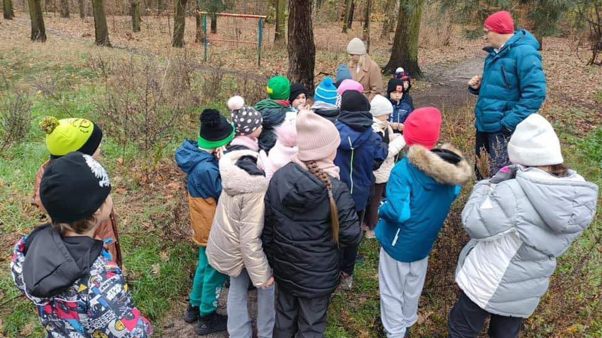 Grupka dzieci w lesie słucha nauczyciela