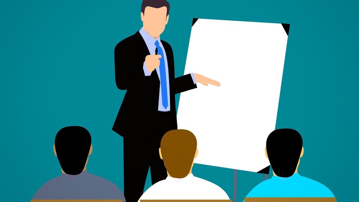 grafika, jedna osoba stoi przy tablicy, trzy siedzą tyłem