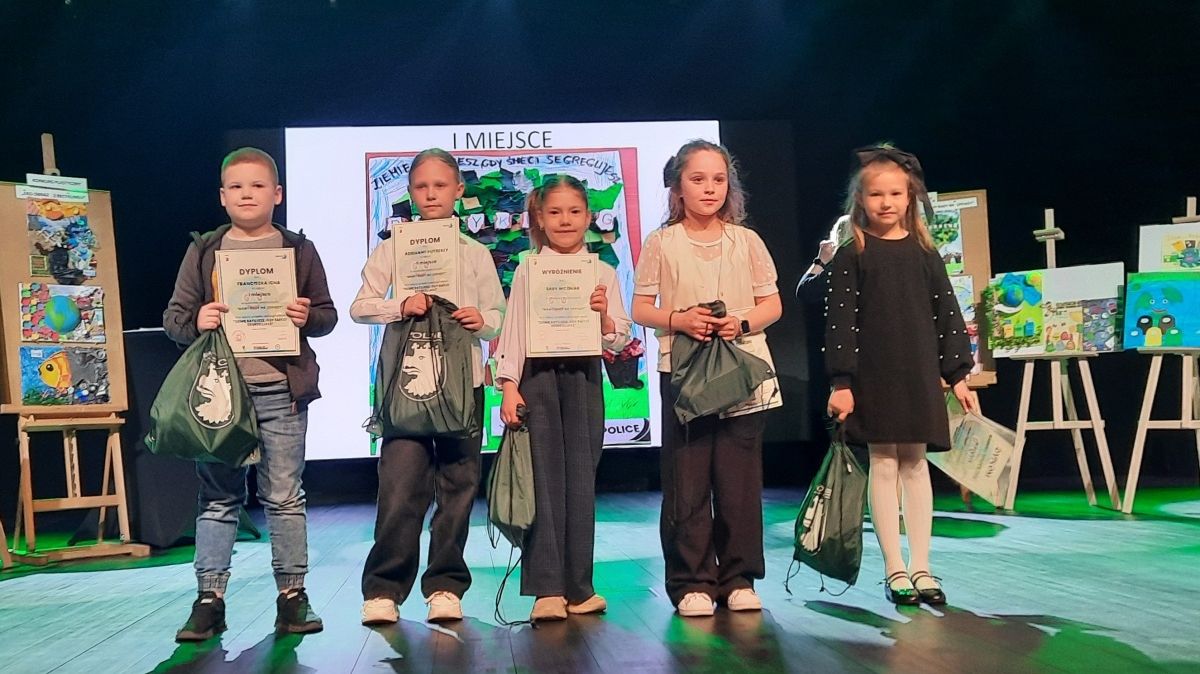 Piątka nagrodzonych dzieci stoi na scenie trzymając worki z nagrodami, po bokach na sztalugach prace uczestników konkursu