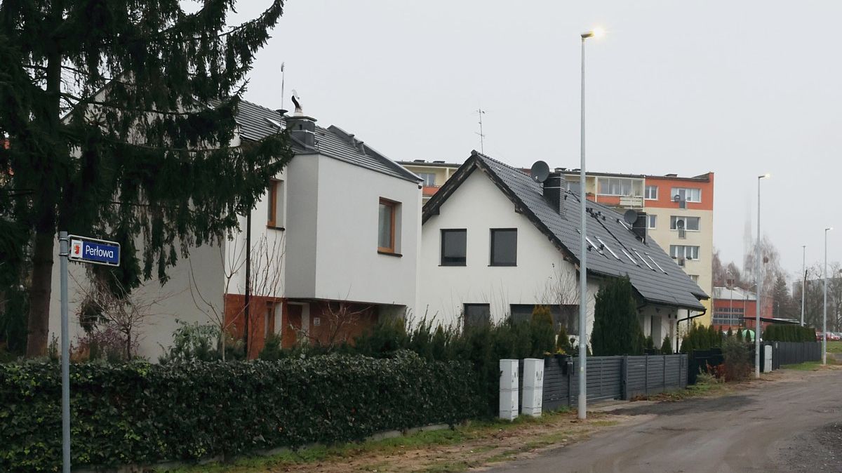 Na zdjęciu ulica Perłowa . Widoczne zapalone lampy, przy ulicy dwa domki jednorodzinne, w tle budynek wielorodzinny