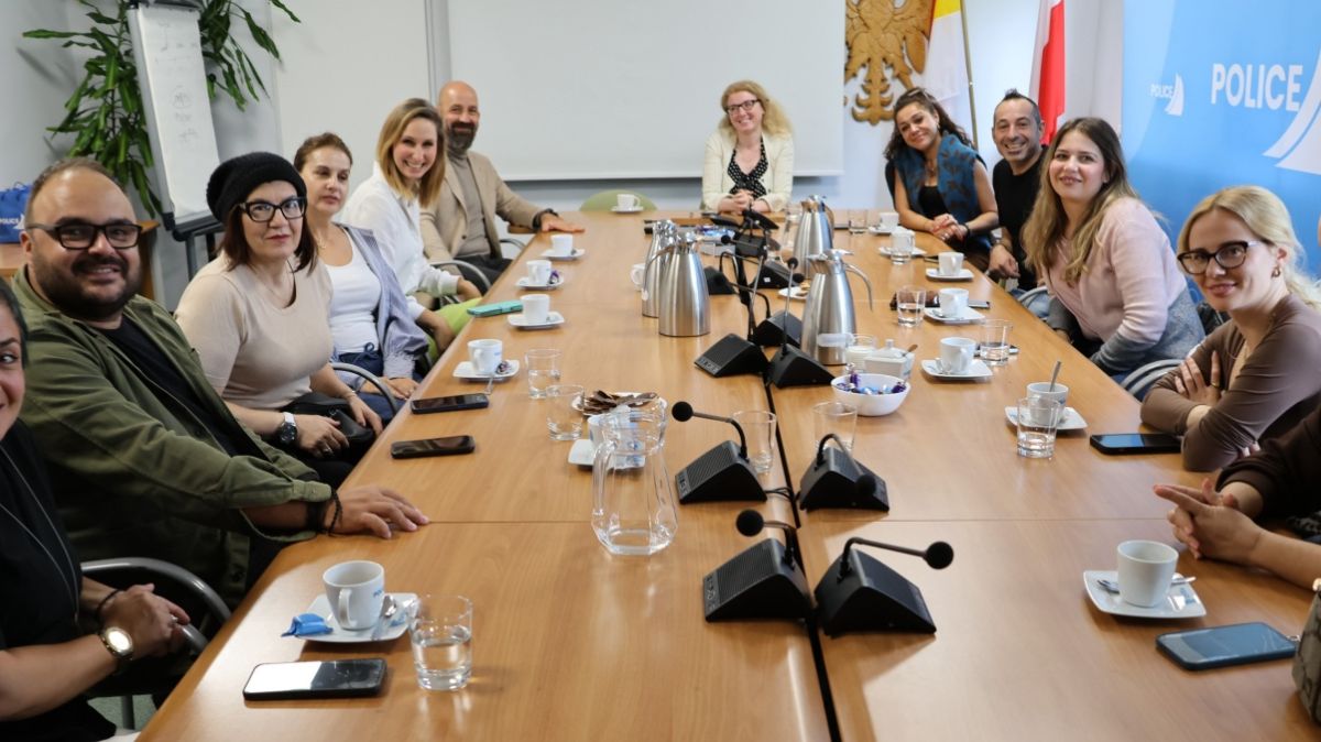 Osoby siedzą przy dużym stolę, patrzą w stronę osoby fotografującej