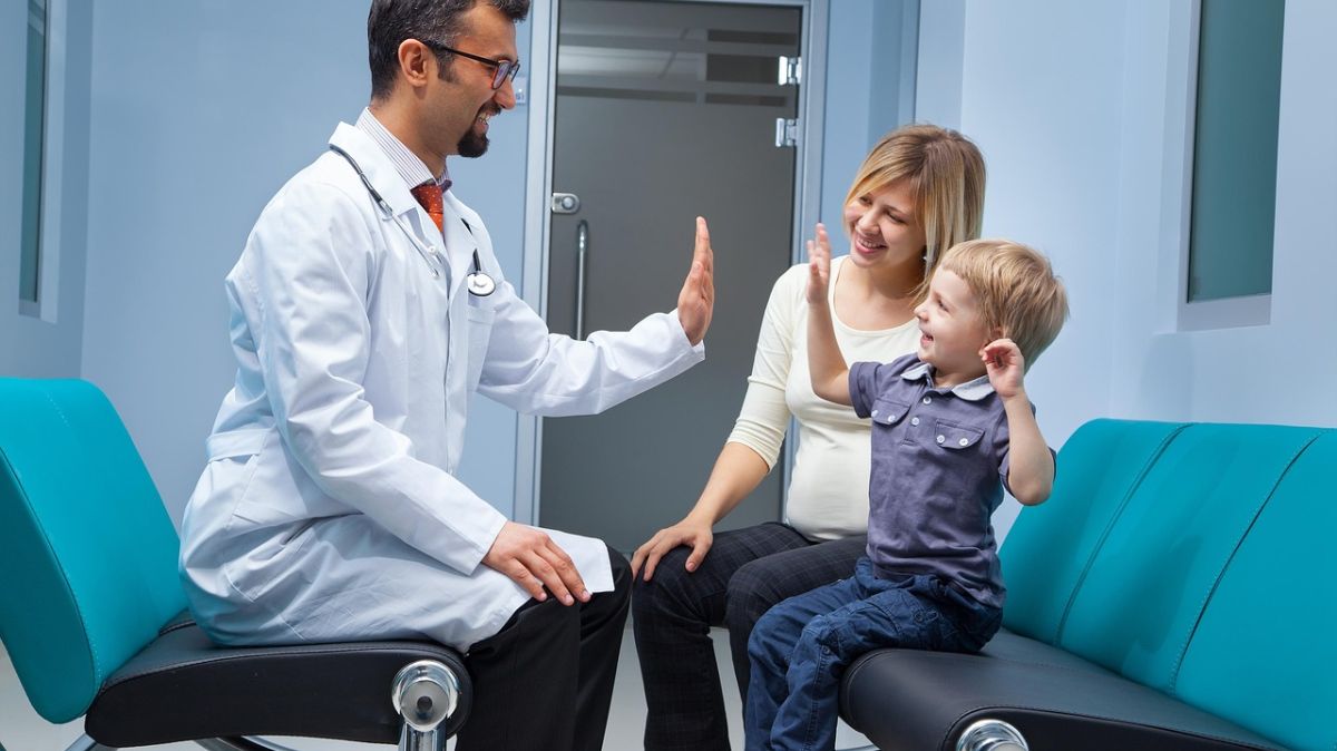 Lekarz przybijający "piątkę" z dzieckiem, obok siedzi mama