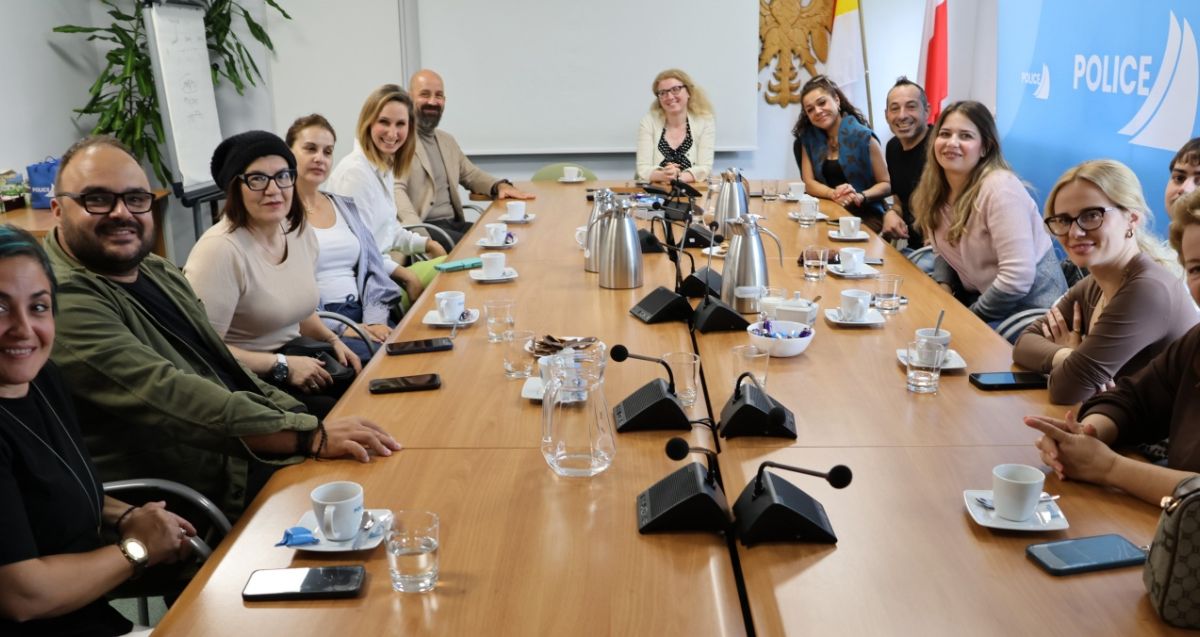 Osoby siedzą przy dużym stolę, patrzą w stronę osoby fotografującej