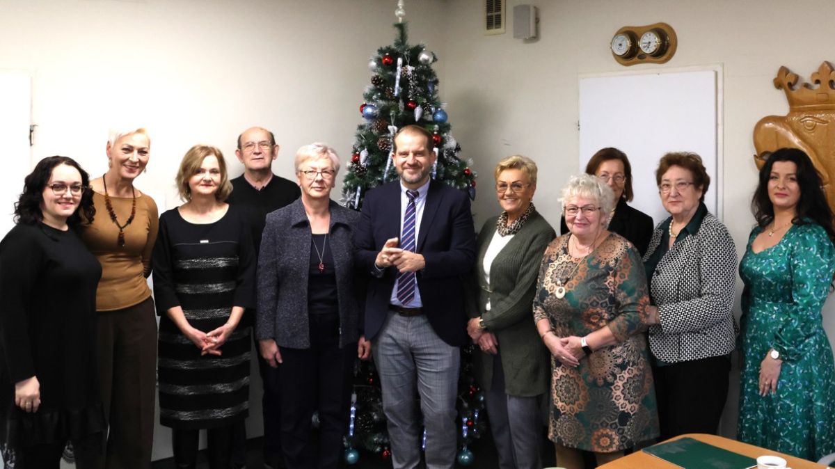 Na zdjęciu 11 osób w tle na środku stoi choinka