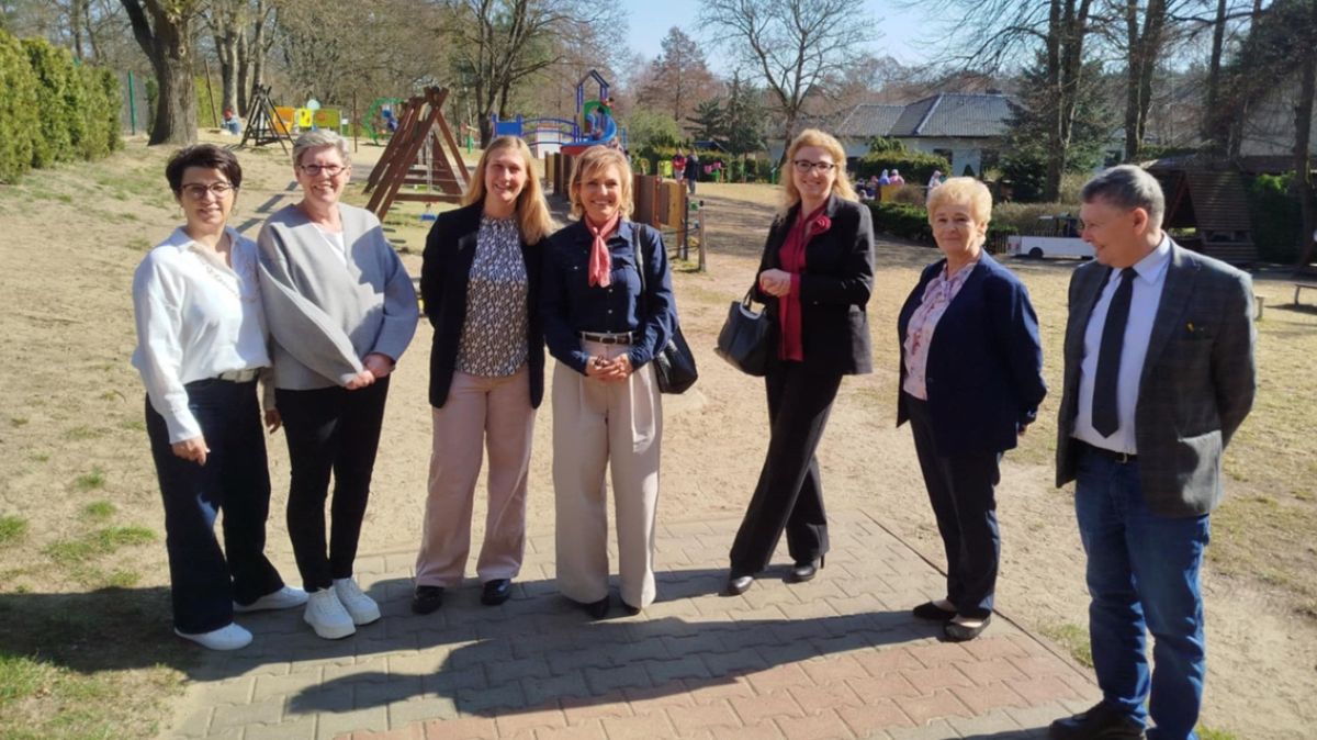 Siedem osób pozuje do zdjęcia. W tle plac zabaw