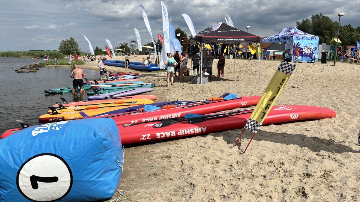 Na plaży leżą deski i sprzęt wodny, w tle osoby