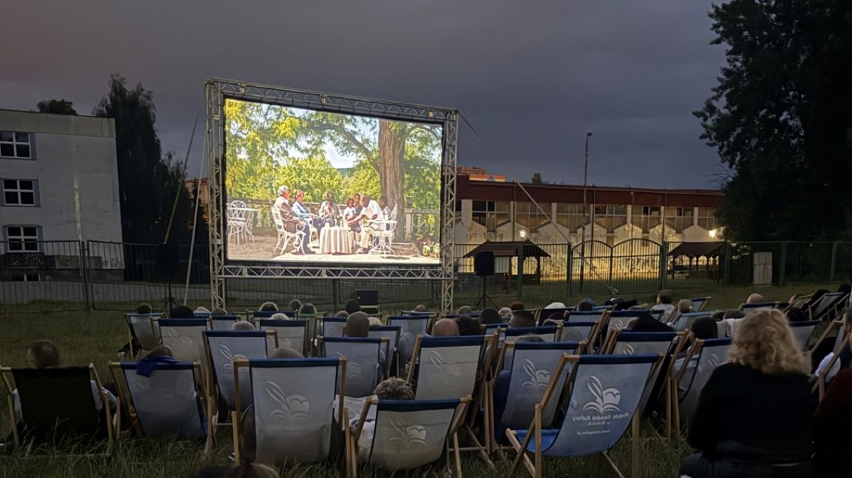 Seans kina - w tle ekran, na pierwszym planie osoby siedzące na leżakach