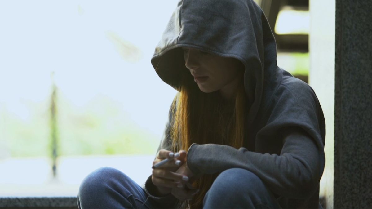 Młoda dziewczyna siedzi na parapecie z papierosem w ręku