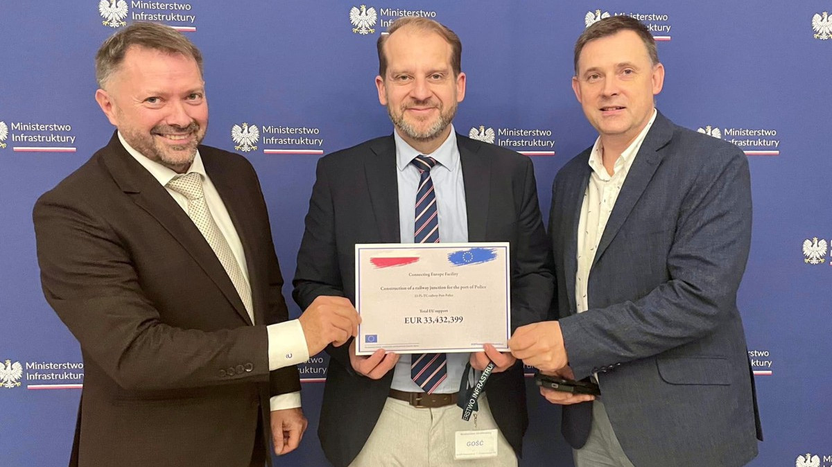 Trzey osoby stoją i trzymają tabliczkę z dofinansowaniem