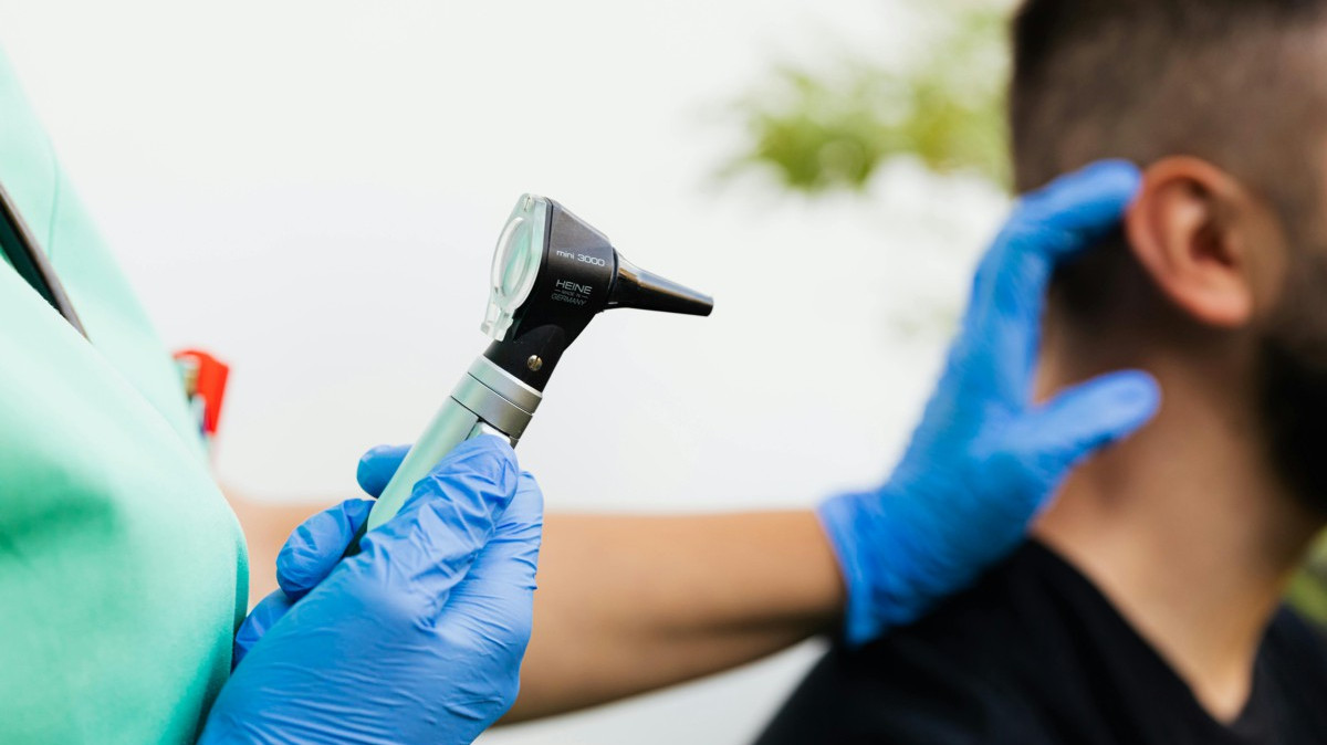 Część głowy mężczyzny i ręka trzymająca przyrząd do badania słuchu