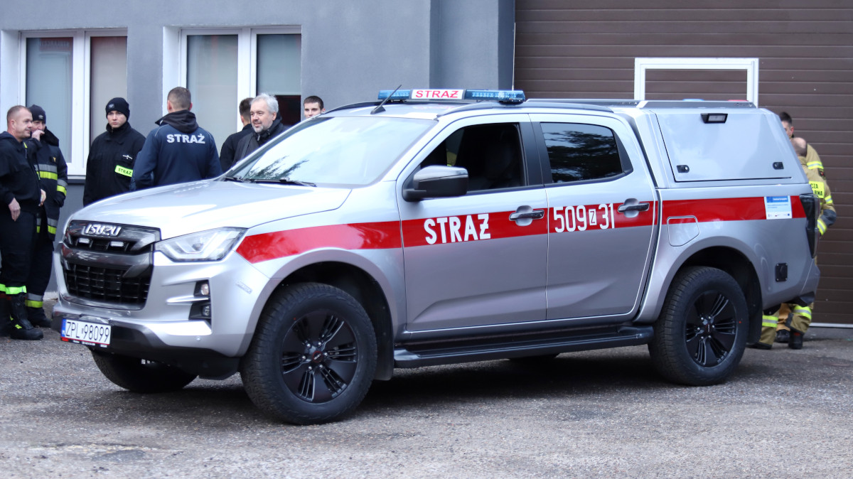 Na pierwszym planie lekki samochód rozpoznawczo-ratowniczy. w tle osoby i budynek remizy w Tanowie