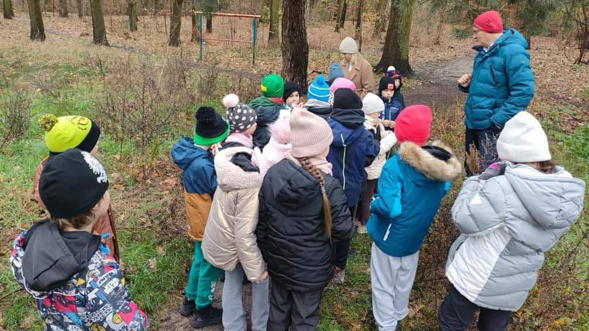 Grupka dzieci w lesie słucha nauczyciela